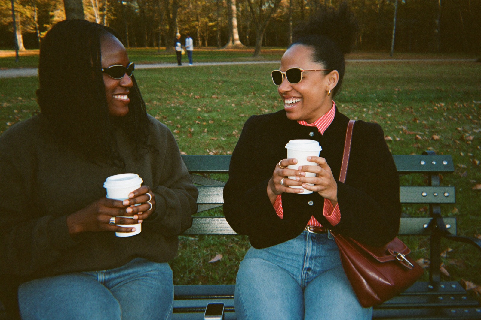 Two friends laughing on a park bench with coffee